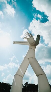 Vertical video of air white dancer against sunny blue sky with clouds. Funny toy character moves actively due to rising air, attracting attention.