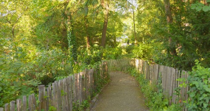 Profile view dirt path framed with wooden fence with lush, green foliage during daytime of Botanical garden in Toulouse, France.