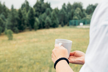 womans hands, enjoying drink while standing in front of forest, wet cup and soft lighting emphasize calm atmosphere, concept of nature retreat, slow lifestyle