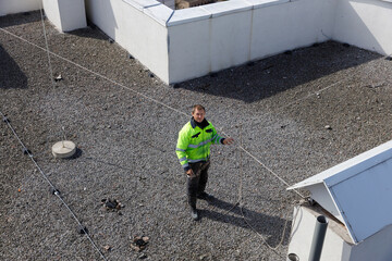 Worker in Safety Gear on Rooftop: Ensuring Safety Protocols While Using Guiding Rope and Secured...