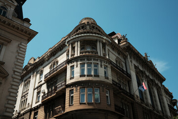 Historic corner building in Belgrade with ornate facade, columns, balconies, and Serbian flag under...