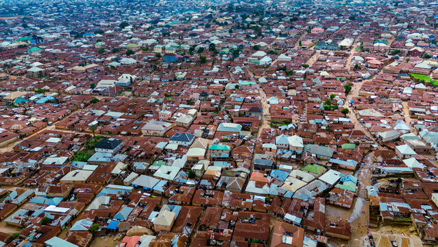 Aerial view of a densely packed urban landscape with rust-colored rooftops contrasting against the blue sky, creating a textured tapestry of human habitation, Jos, Plateau, Nigeria.