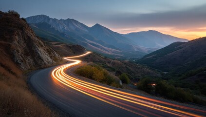 Winding Mountain Road Illuminated by Vehicle Lights at Dusk with Majestic Silhouette Mountains.