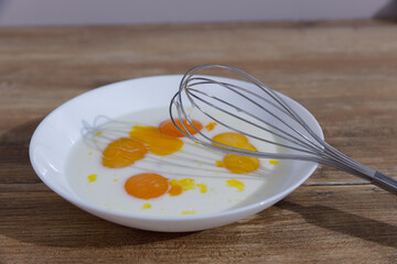 A Close-Up View of Fresh Eggs Whisked Together with Milk in a White Bowl on a Rustic Wooden Surface for Delicious Culinary Creations and Homemade Recipes