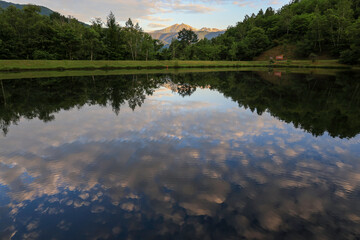 Early morning view at Takasome Camp, Nagano, with Mount Norikura and sunrise clouds beautifully mirrored in a calm lake surface.
