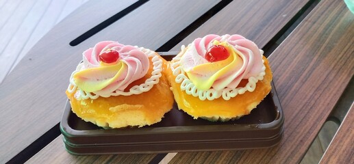 Retro style orange cupcake on plastic plate on wood table and decorated cream and jelly on top.