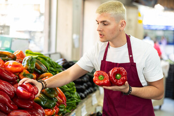 Male salesperson carefully places ripe bell peppers on a display case at a grocery supermarket