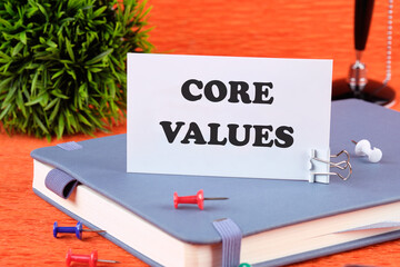 CORE VALUES word written on a business card standing with a clip on a diary, a notebook on an...