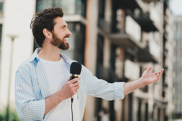 Handsome urban man holding a microphone outdoors during a sunny day in the city portraying happy...