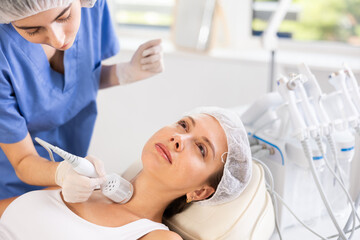 Young female cosmetologist performs hardware whitening procedure on neck of young female patient