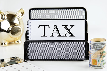 TAX text on a white piece of paper next to a piggy bank, a roll of money and a calculator on a...