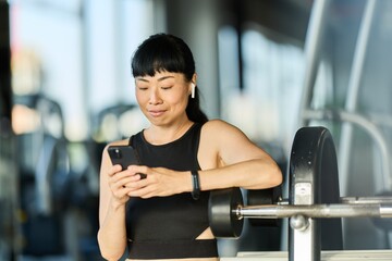 Woman Using Smartphone and Earbuds While Exercising at Fitness Gym