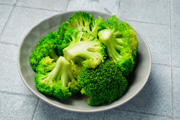 Boiled green broccoli in a bowl. On a light kitchen table. Preparing healthy diet food.