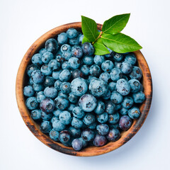 Wooden bowl with fresh blueberries and green leaves. On a white background, close-up, macro.