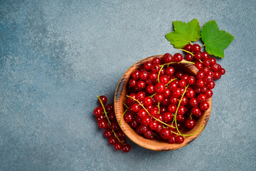 Sprigs of red currant in a round wooden bowl. On a gray stone background.