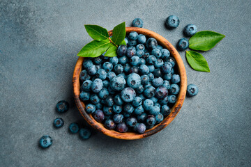 Wooden bowl with fresh blueberries. Close-up, free space for text. On a stone background.