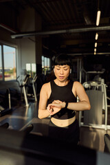 Woman Running Indoors at Gym While Checking Fitness Device on Her Wrist