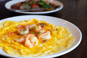 Delicious shrimp omelette served on a white plate. Freshly cooked eggs with juicy shrimp, perfect for breakfast or brunch. Tasty Asian-style seafood dish on wooden table
