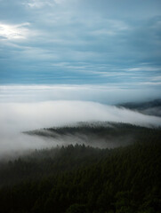 A serene view of mist rolling over lush green hills beneath a cloudy sky creates a peaceful and enchanting atmosphere. Generative AI.