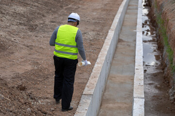 An Asian civil engineer in safety gear supervising a construction project by a railway.