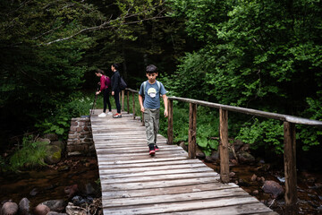 Family hiking in forest crossing wooden bridge over creek