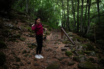 Fototapeta premium Young female hiker adjusting backpack on rocky forest trail