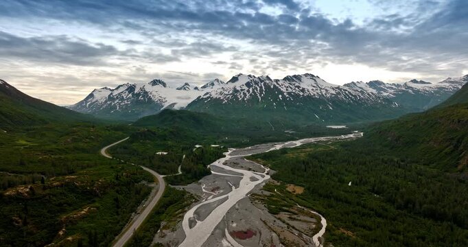 Overcast grey sky over the stunning nature landscape. Drone flight over the branched river in the valley among the picturesque mountains. Alaska wilderness.
