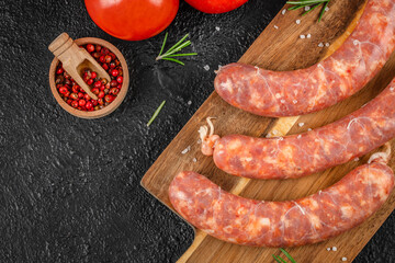 Raw pork sausages with visible fat marbling lie on a wooden board next to coarse salt, red...
