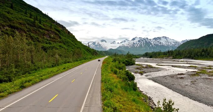 Following a car moving by the road along the delta of the dried up river. Jaw-dropping view of the mountains in Alaska from drone.