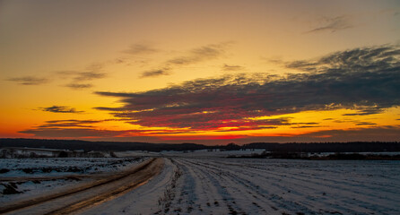 Beautiful winter landscape with snow-covered field and road at sunset