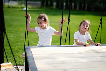 Two young girls in white dresses playing on a swing set outdoors
