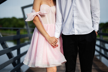 Couple holding hands on scenic bridge wearing stylish elegant outfits