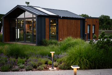 Modern small house with wooden facade and garden landscape around during evening