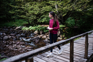 Obraz premium Young girl walking on wooden bridge exploring forest river hiking trail