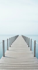 Fototapeta premium Wooden pier extending into calm ocean under pale sky view