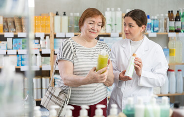 Mature woman holding medicated shampoos for hair restoration in her hands and consulting pharmacist...