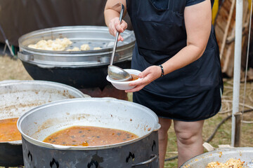 A woman is serving food from a large pot to a bowl