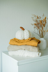 Knitted autumn sweaters on chest of drawers in home interior with pumpkins decor. Home organization.