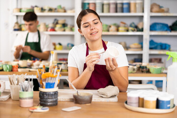 Young woman painting clay ceramic cup in workshop