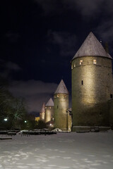 Outside of the Tallinn old town fortified walls with light shining on the towers and white snow illumination the ground on winter evening, Estonia