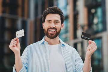 Confident man in stylish casual outfit outdoors showing credit cards in an urban setting during...