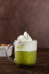 Green tea matcha latte with pistachio in a glass on brown background. Vertical orientation.