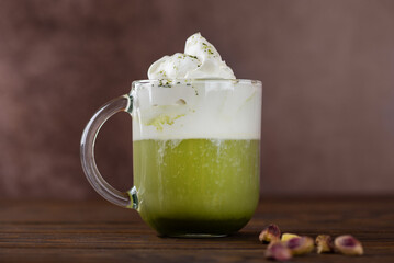 Pistachio green tea latte, Japanese matcha latte, with whipped green tea and cream on brown wooden table.