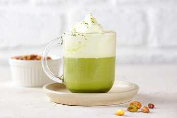Vegan pistachio green matcha latte tea in a glass on a white table. Healthy drink.