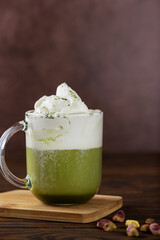 Pistachio matcha latte tea in a glass on a wooden board. Vertical orientation.