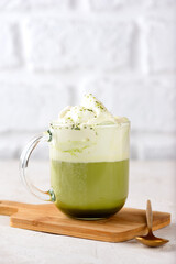 Green tea matcha latte with whipped coconut milk and pistachio on wooden board. Vegan drink. Vertical orientation.