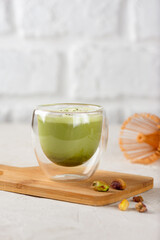 Pistachio matcha latte with coconut milk in a glass on a wooden board. Vertical orientation.