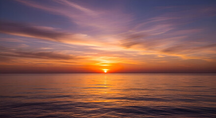 Obraz premium Wide shot of a tranquil sunset over a calm body of water. The sky displays a mix of orange, pink, and purple hues, while the water reflects the colors of the sky.