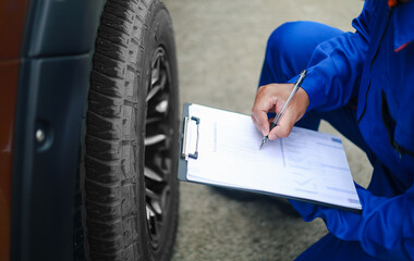 Auto mechanic is writing on clipboard. Mechanic is making checklist and checking condition of car tire. Concept of car service, repair, maintenance.
