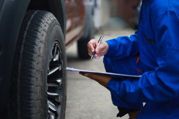 Auto mechanic is writing on clipboard. Mechanic is making checklist and checking condition of car tire. Concept of car service, repair, maintenance.